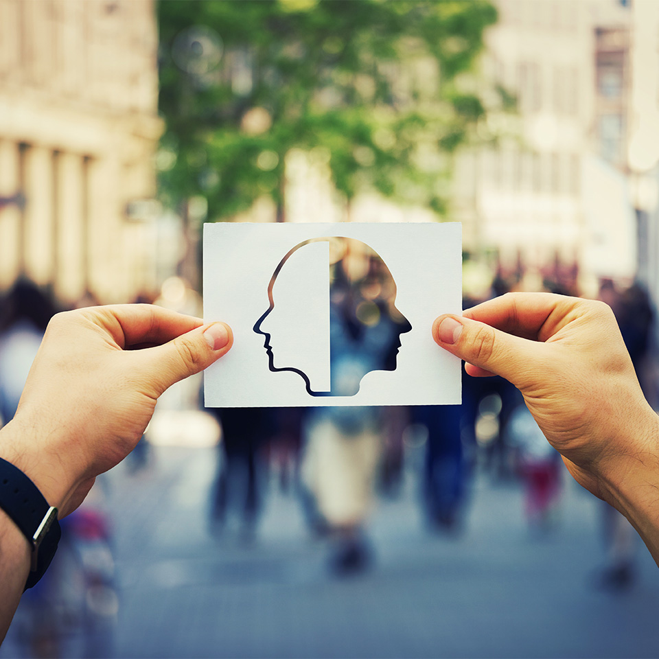 Pair of hands holding up an illustration of two heads facing away from each other
