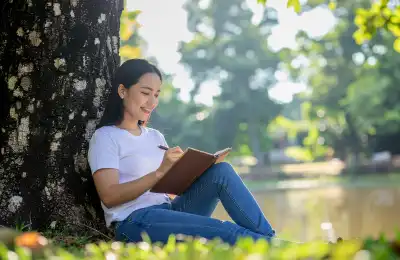 woman writing in journal outside undre tree