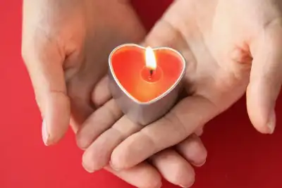 Someone holding a lit heart shaped tea light in their hands