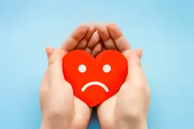 Hands holding a red love heart with a sad face on