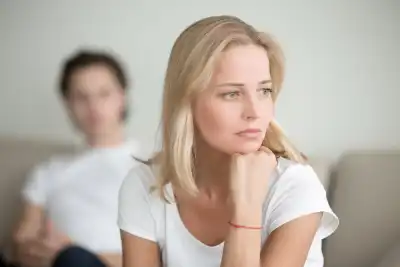 Woman looking sad staring into the distance with her partner blurred out behind her