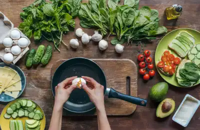 Someone cooking vegetables and cracking an egg into a pan.