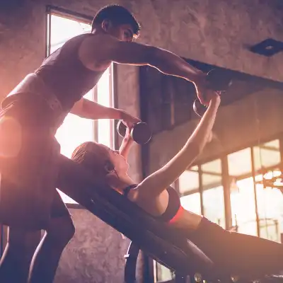 Woman doing weight exercises in a gym with the assistance of her personal trainer