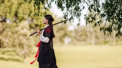 Female Samurai holding a sword with greenery in the background.