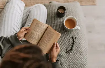 person reading a book with a cup of tea and candle