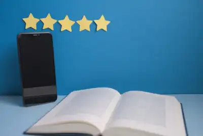 An open book next to a phone with 5 stars on the wall