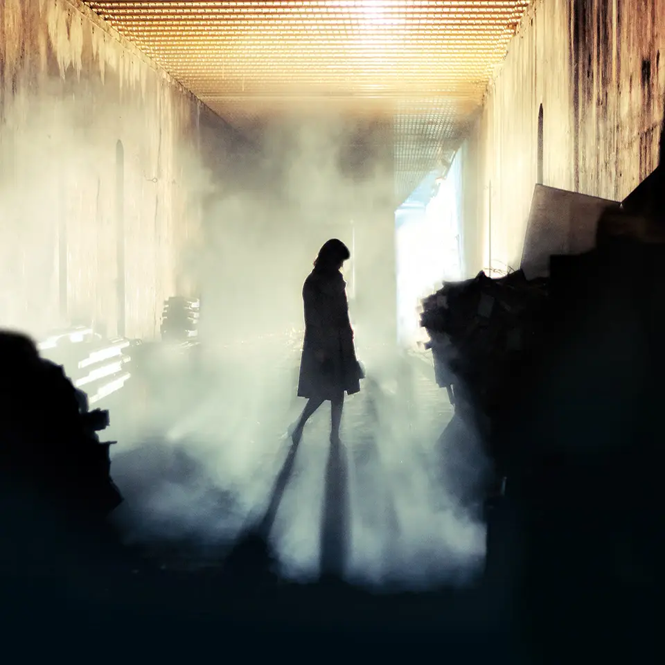 A silhouetted figure walking across a mist-filled corridor