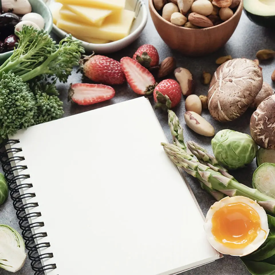 Healthy, Ketogenic diet ingredients on a table, alongside a blank pad, ready for meal planning
