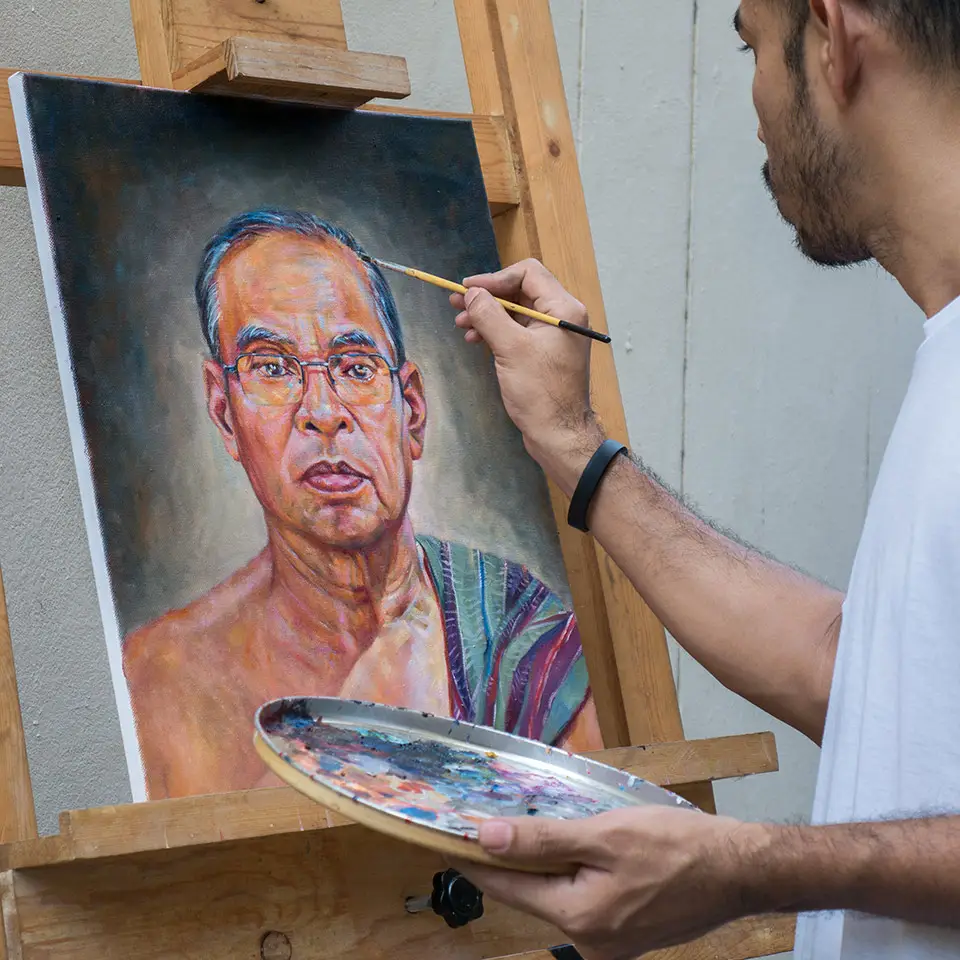 Artist painting portrait of a man using oil colour on a canvas, which is on an easel