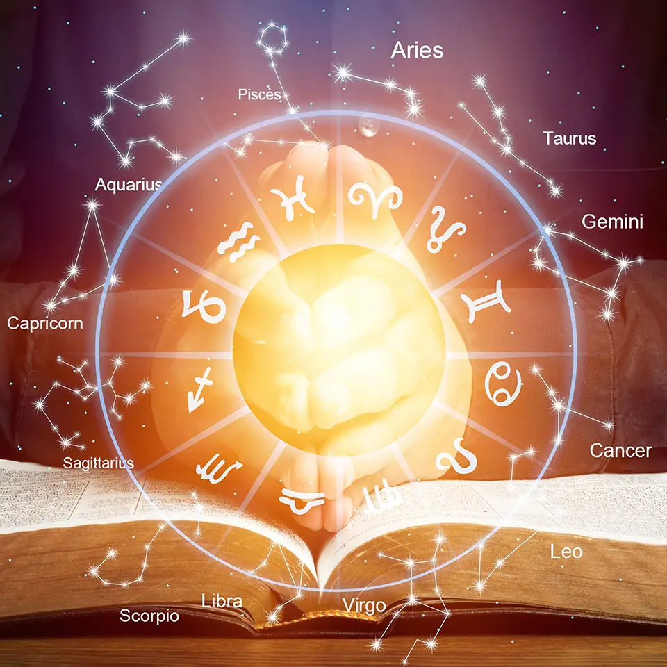 Astrological signs and zodiac symbols surrounding a glowing circle in front or a pair of hands resting on a book