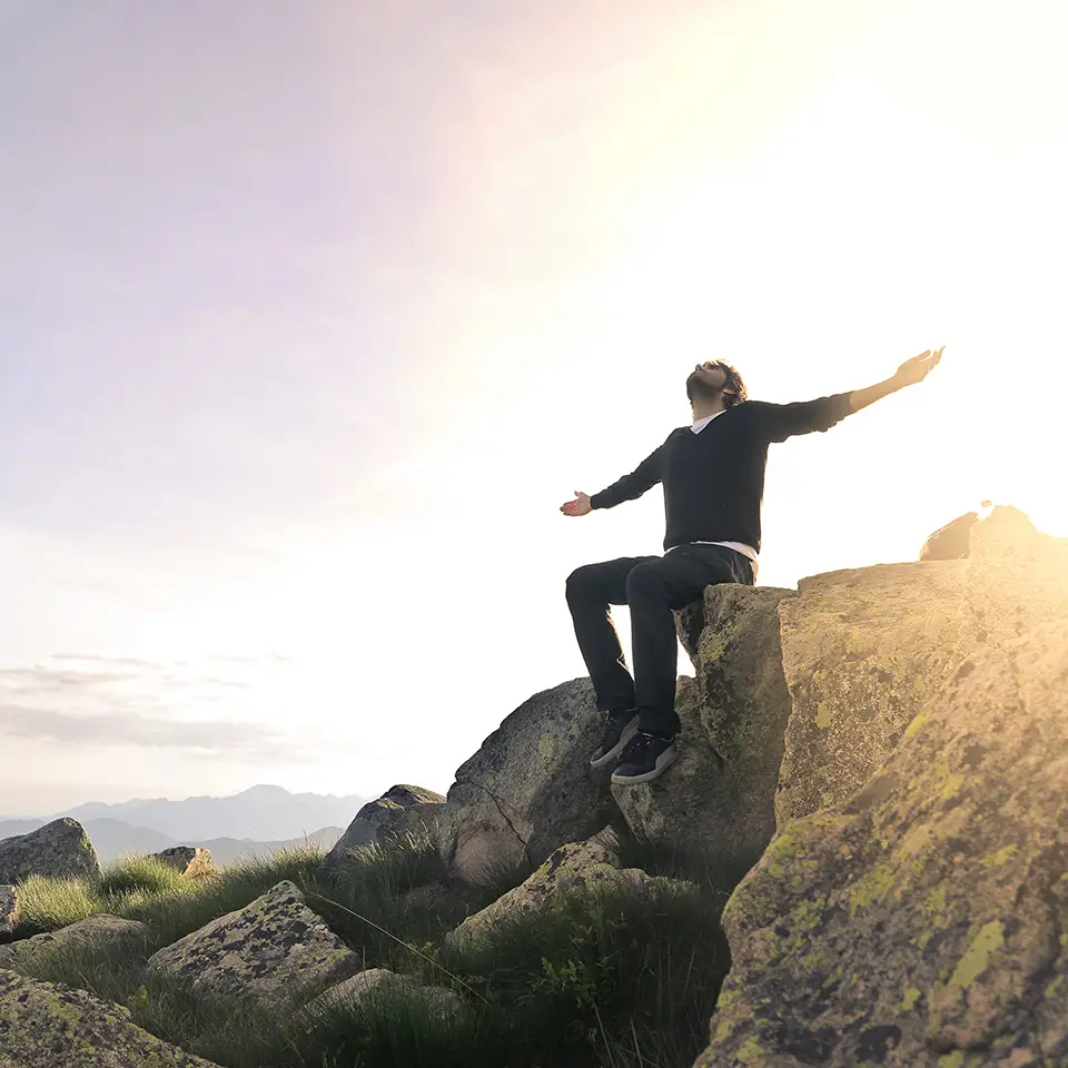 Man feeling free of anger, sitting on top of a mountain with the sun rising behind his back