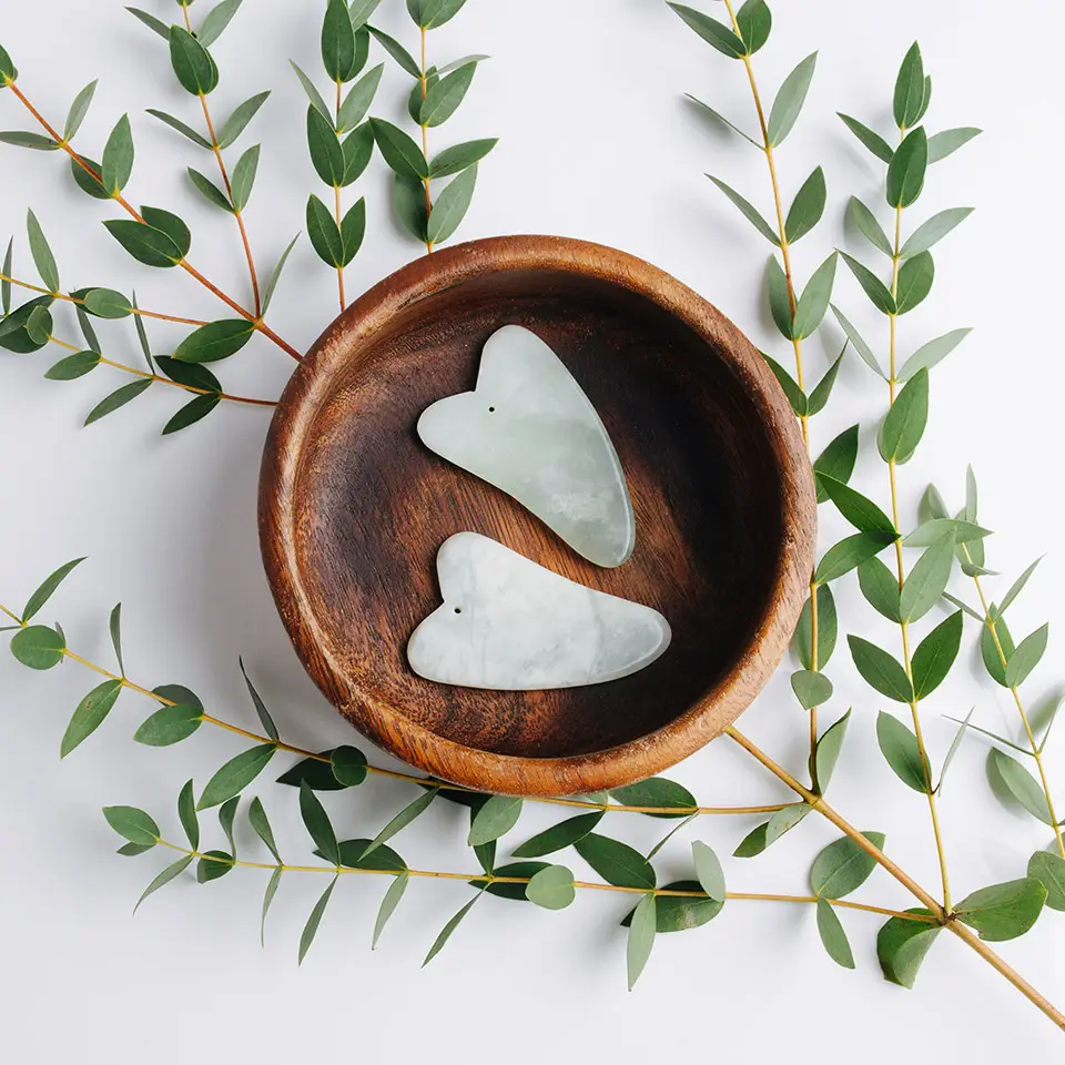 Top view of Gua Sha river stones inside a wooden bowl, decorated with an olive branch