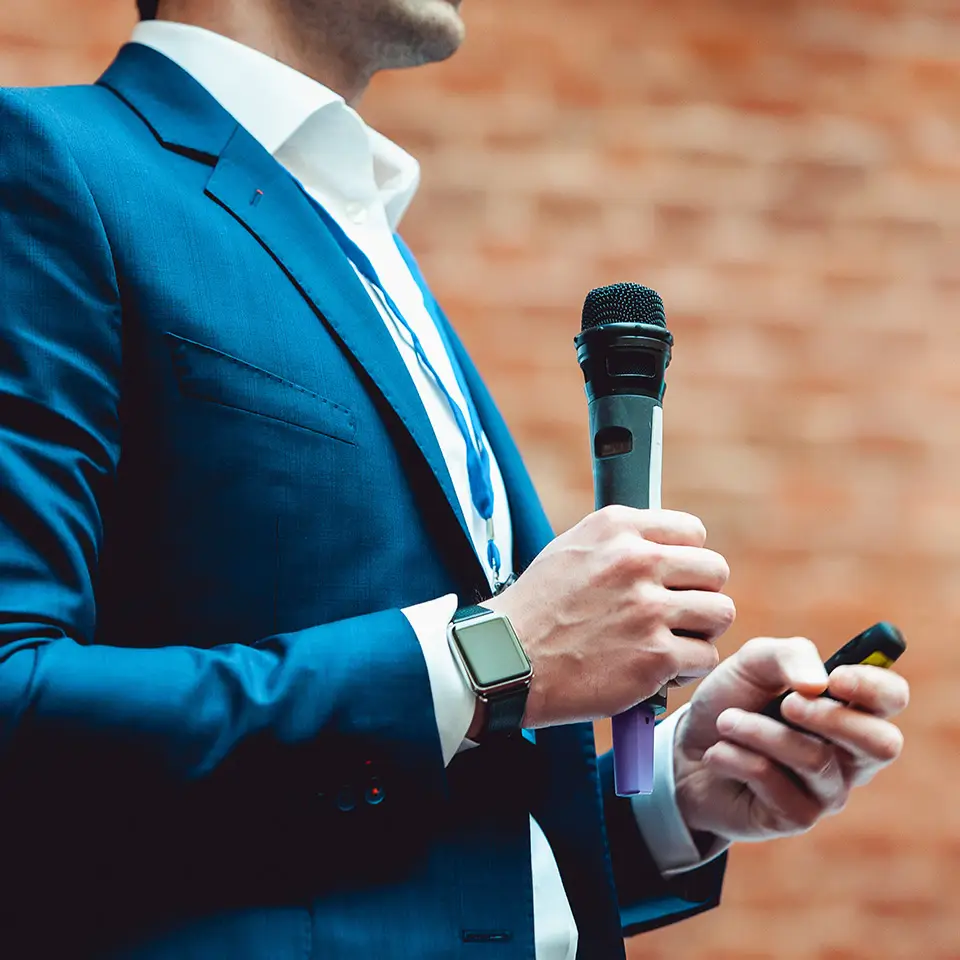 Man in a blue suit holding a gray microphone and making a speech