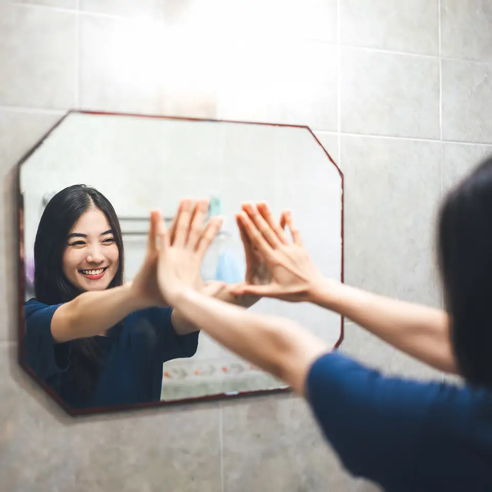 A woman with her hands pressed against a mirror as she smiles at her reflection