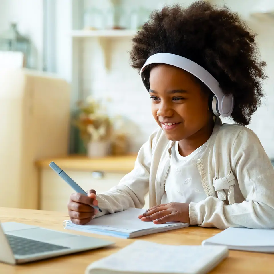 Young child working at a computer and writing in a notepad