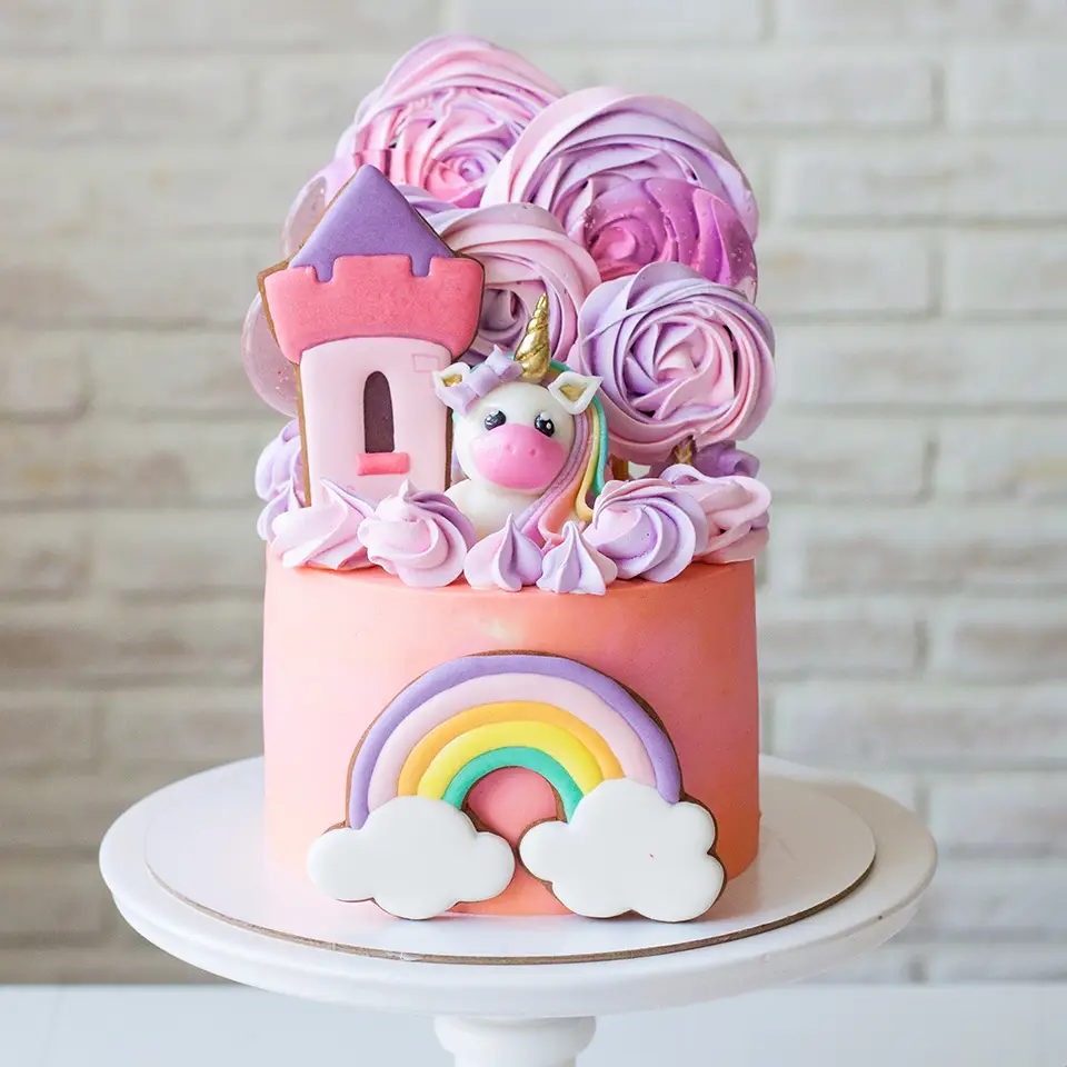 Pink birthday cake with sugarpaste unicorn, gingerbread princess castle, rainbow and meringue clouds
