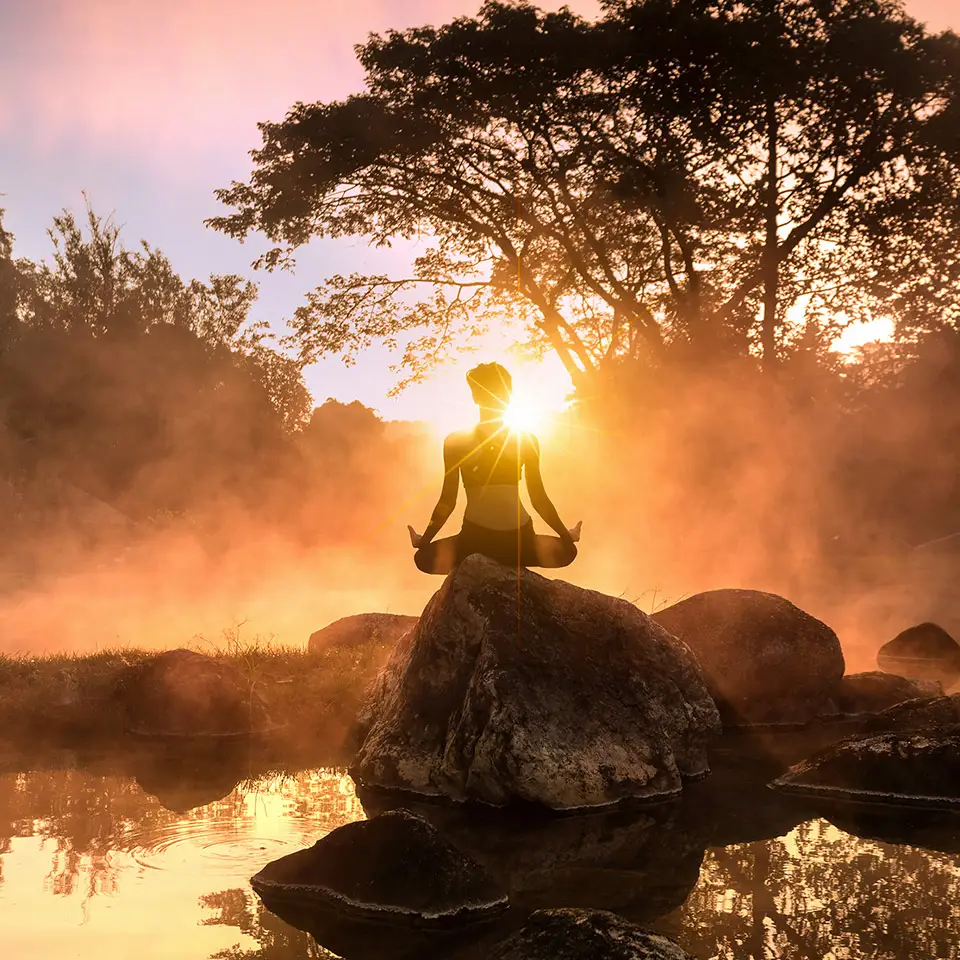 Young woman meditating by a misty lake at sunrise