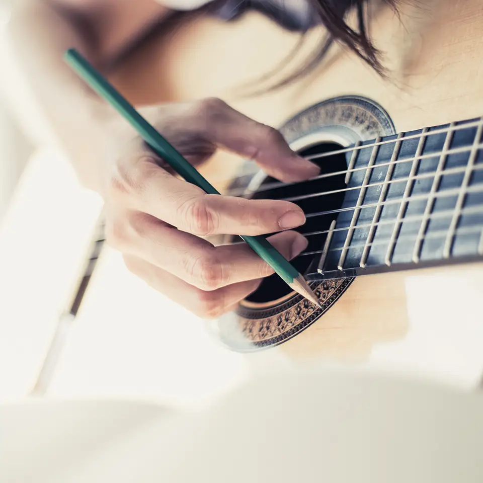 Songwriter playing guitar with a pencil in their hand