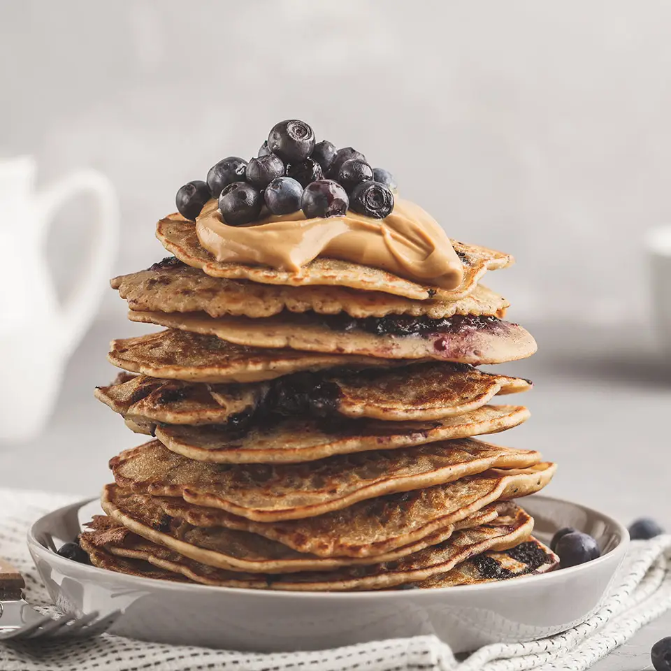 A stack of vegan pancakes with blueberries, peanut butter and syrup