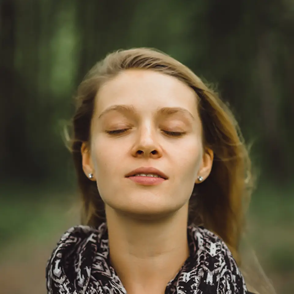 A woman in a forest with her eyes closed and a look of serenity on her face