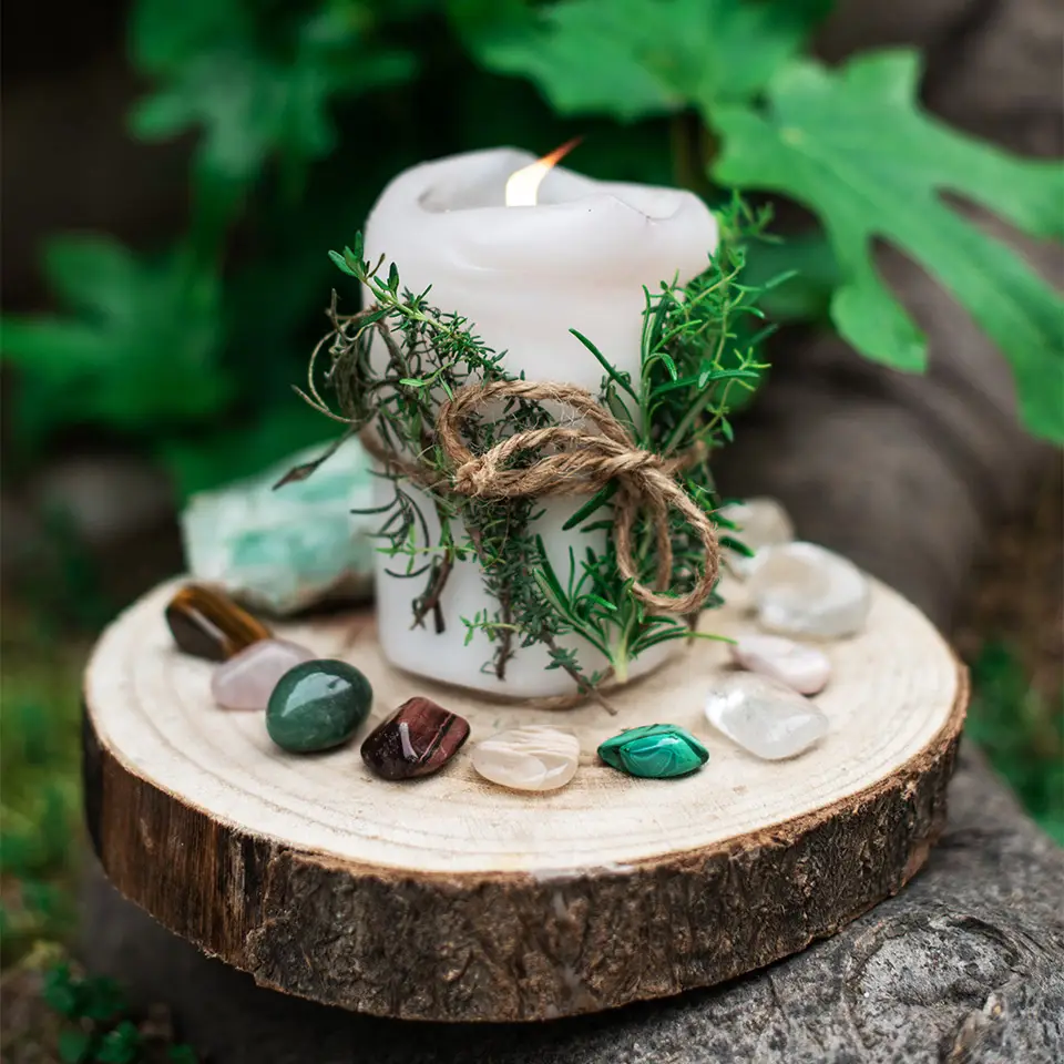 Candle with herbs surrounded by gems and crystals on a wooden log