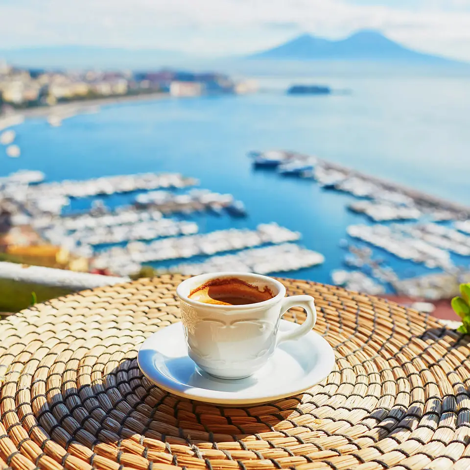 A cup of espresso coffee on a table in front of a view of Vesuvius mount in Naples, Campania, Southern Italy