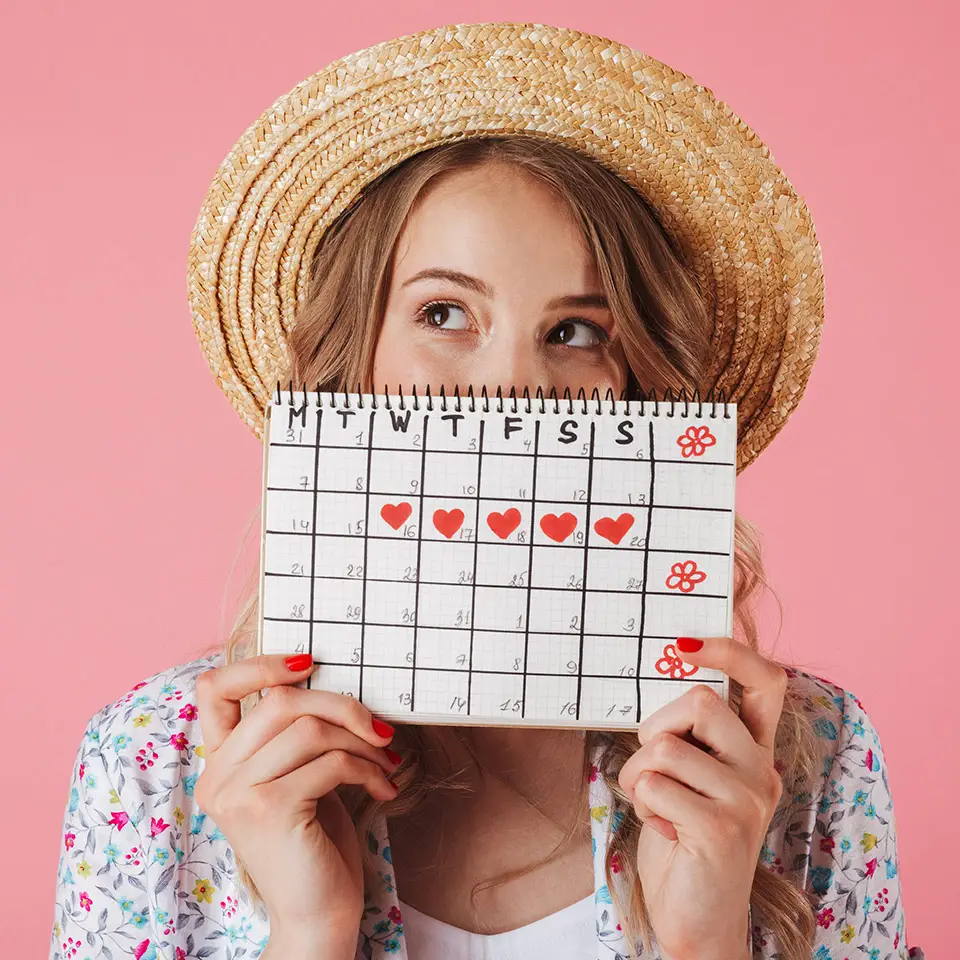Woman in a straw hat holding a menstrual calendar.