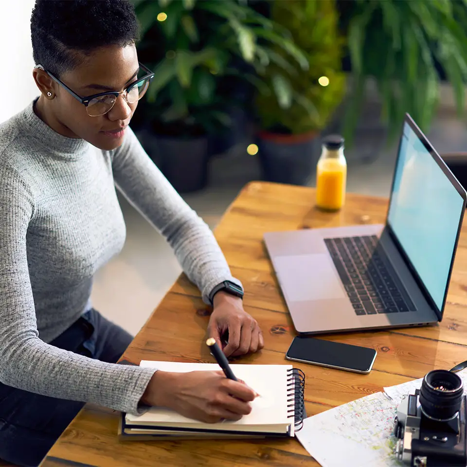 A woman using speed writing to take notes in a notebook whilst at a computer