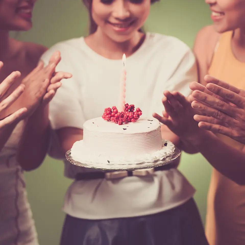 Woman holding a cake with a candle in it as others clap