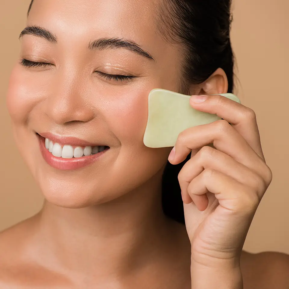 A smiling woman with her eyes closed using a facial Gua Sha jade board