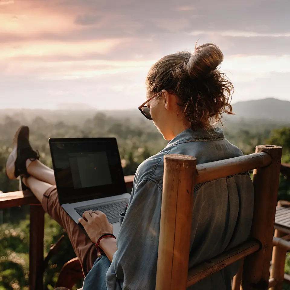A woman remote working at a laptop at sunset or sunrise on the top of a mountain