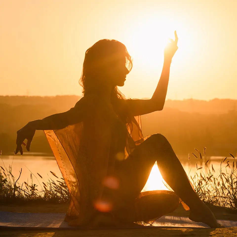 Silhouette of a woman holding a seated yoga pose against a sunrise