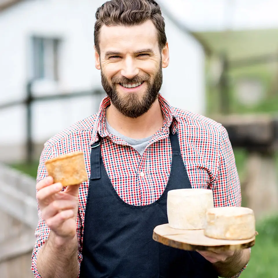 Portrait of a cheesemaker holding a cheeseboard with a collection of homemade cheeses