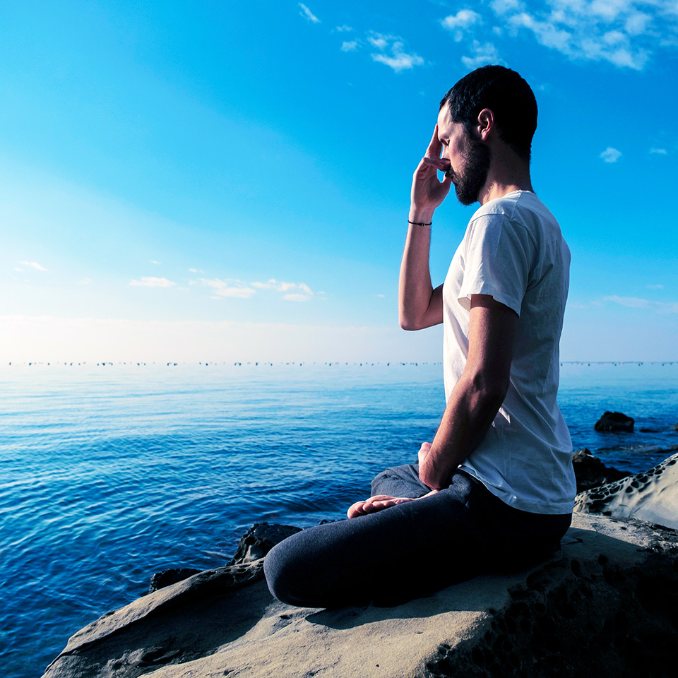 Man practising pranayama breathwork outdoors by the sea.