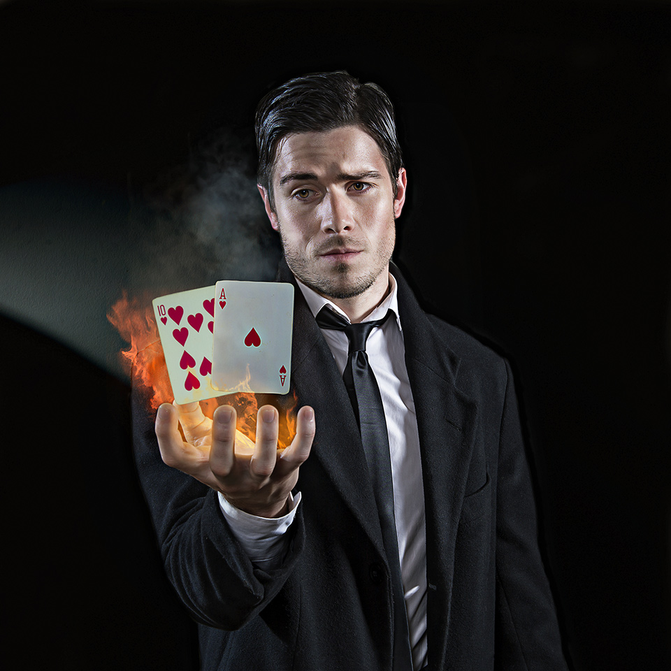 Magician holding their hand out, which is on fire, with two cards levitating above it