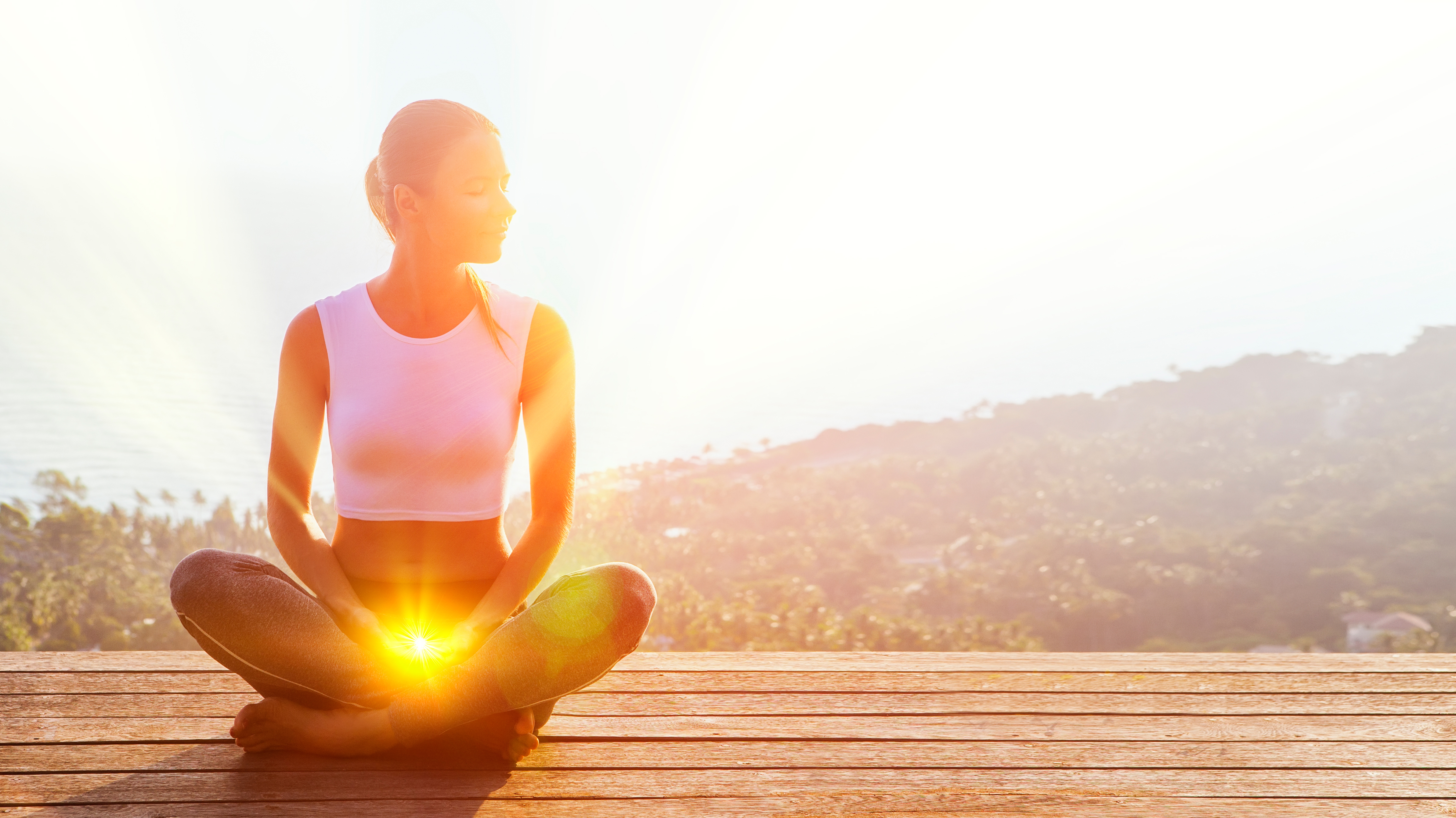 Image of a woman sat outdoors cross legged with the sacral chakra lit up