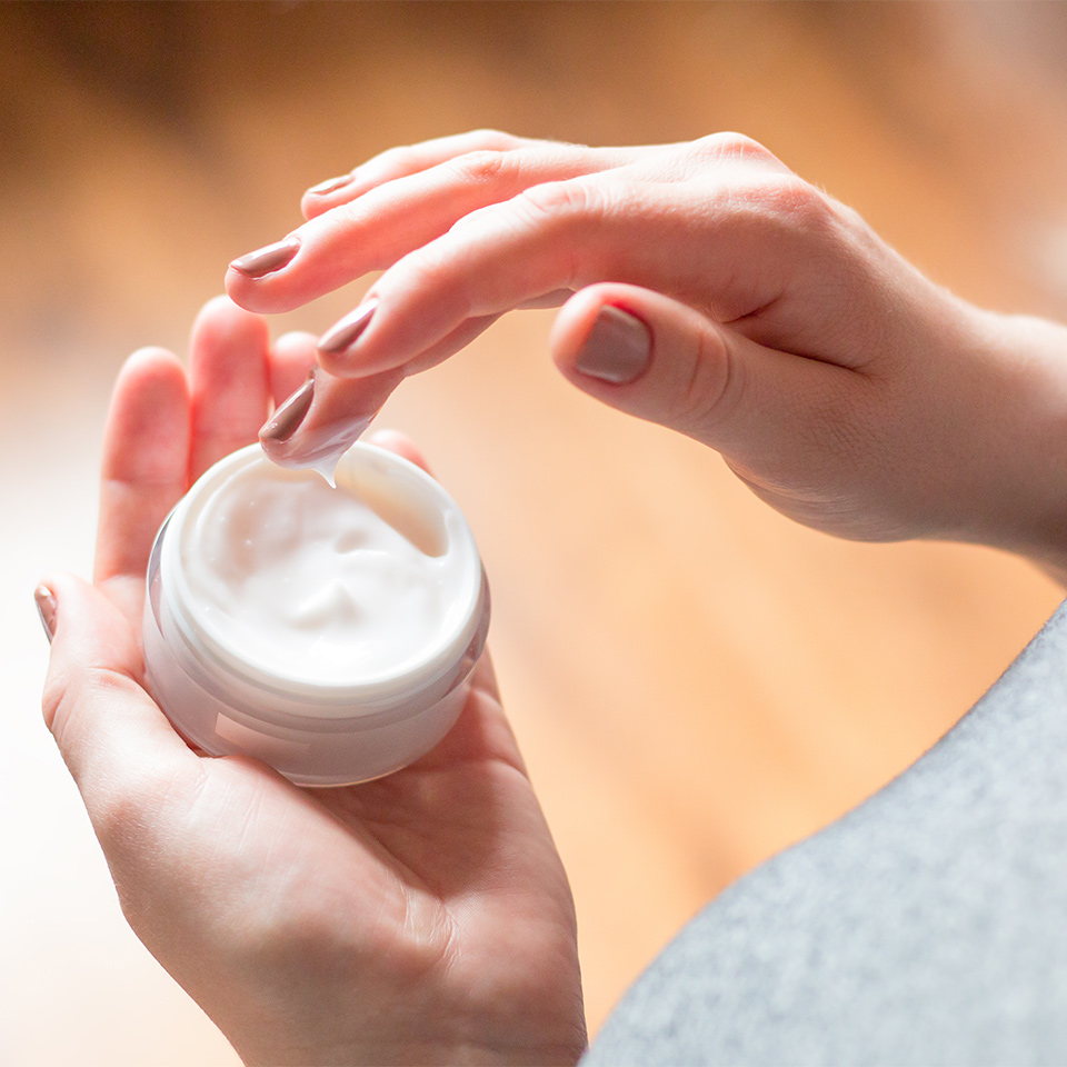 Woman's hand holding a pot of eczema cream, which she is about to use