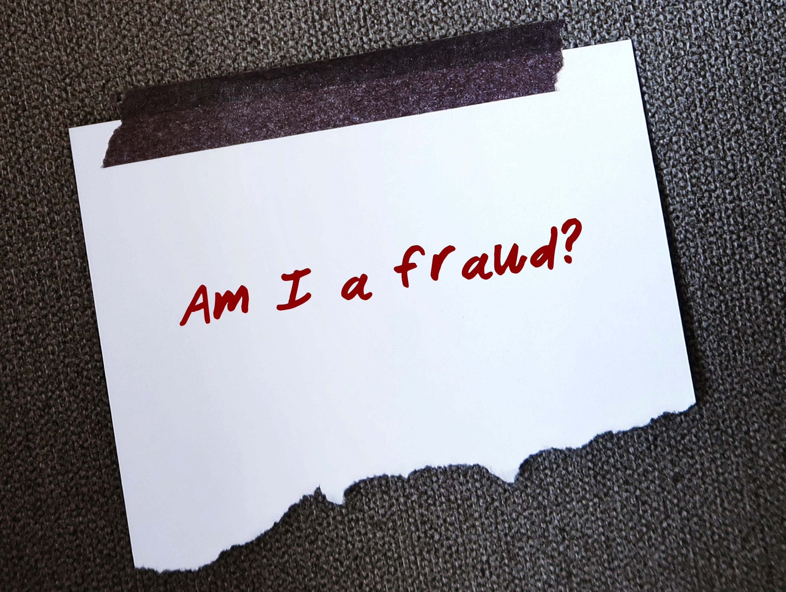 White piece of paper with 'Am I a Fraud?' written on it in red