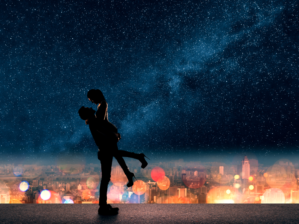 Silhouette of a couple in front of a city skyline and a starry night