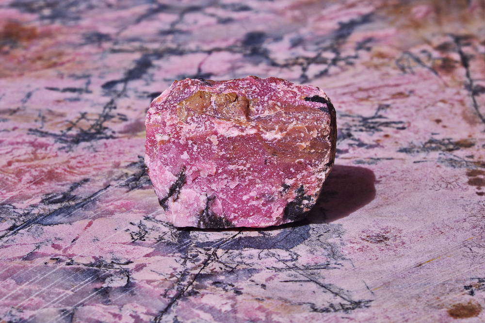 A raw piece of Rhodonite on a Rhodonite slab