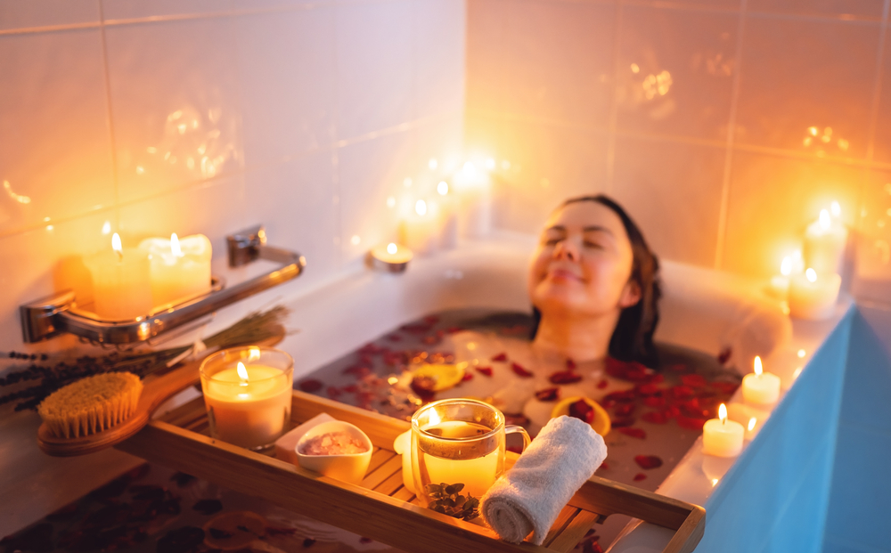 Young woman enjoying spiritual aura cleansing rose flower bath with rose petals and candles during full moon ritual.