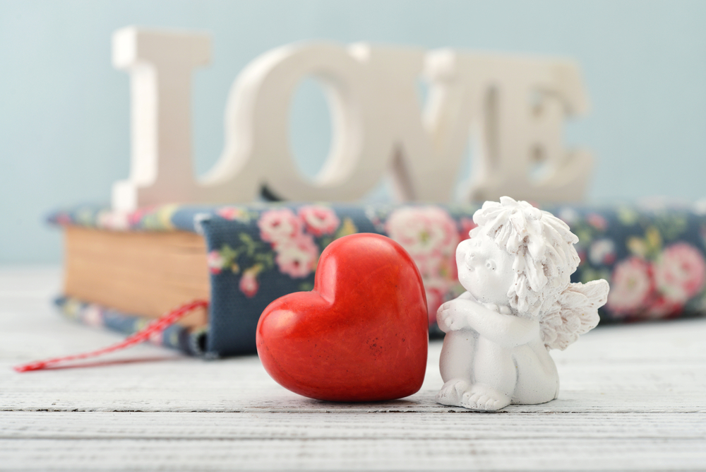 A little angel statue next to a red heart statue