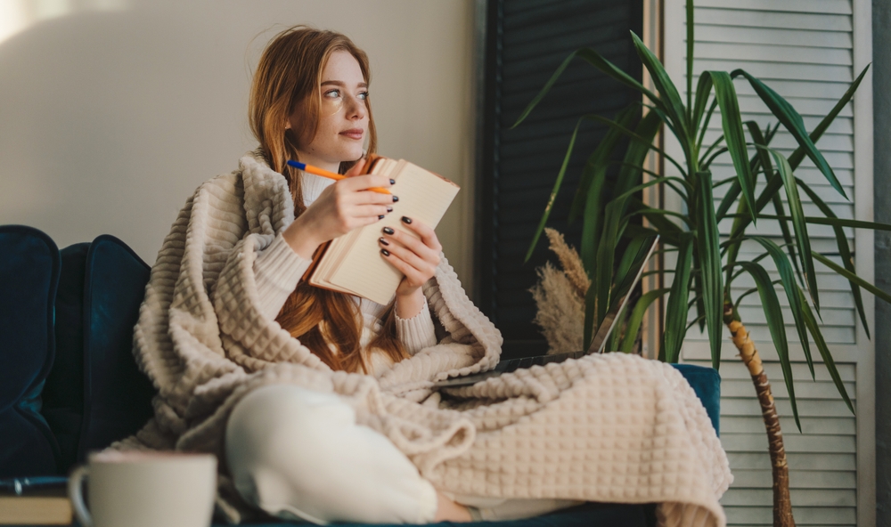 Young woman journalling wrapped in a blanket