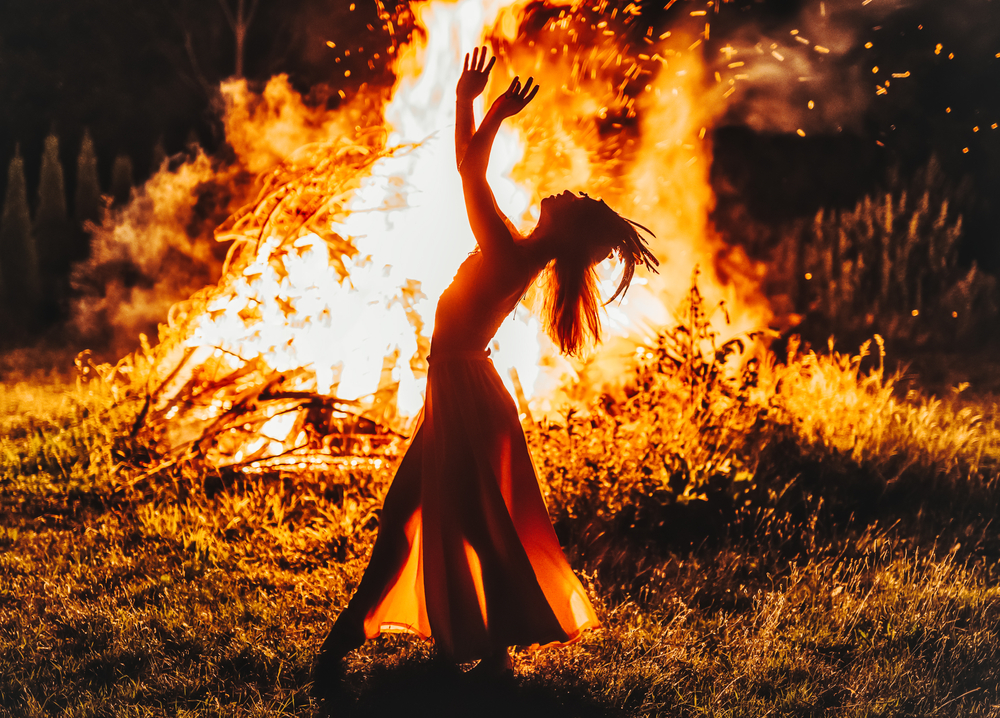 A woman leaning back, head up in front of a large fire