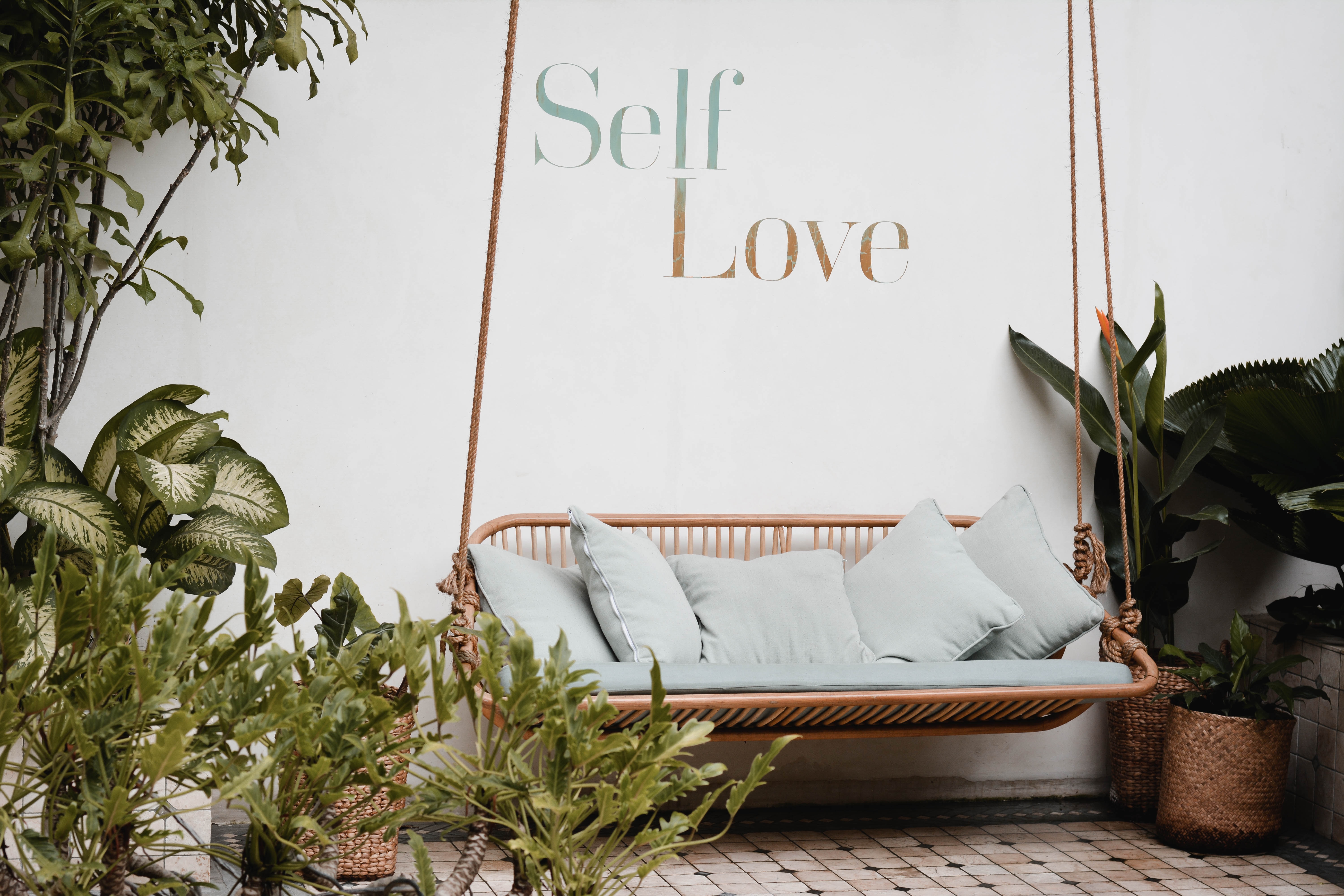 A hanging garden bench with a wall sign that reads "self love" behind it.
