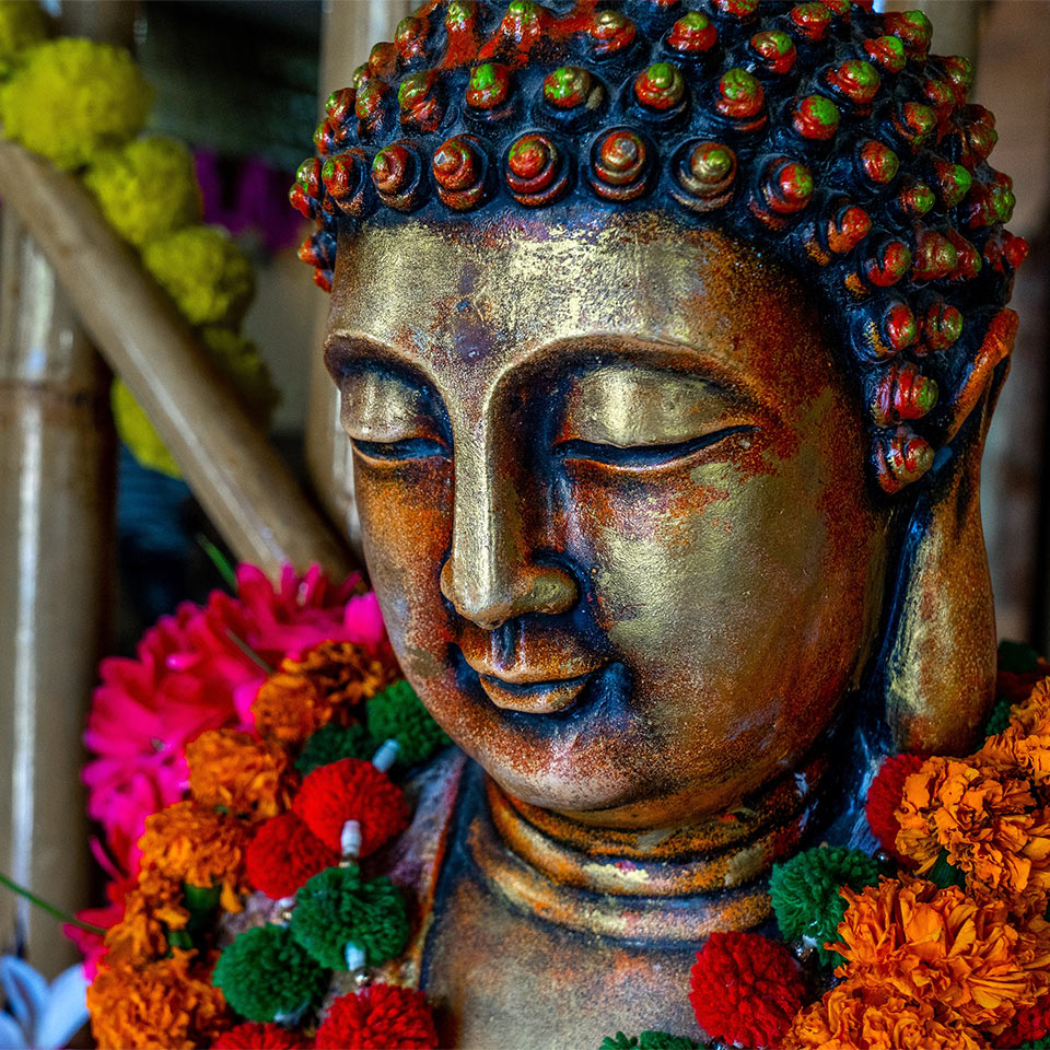 Close up of a bronze buddha statue sitting in meditation dressed with flower decorations for a festival.