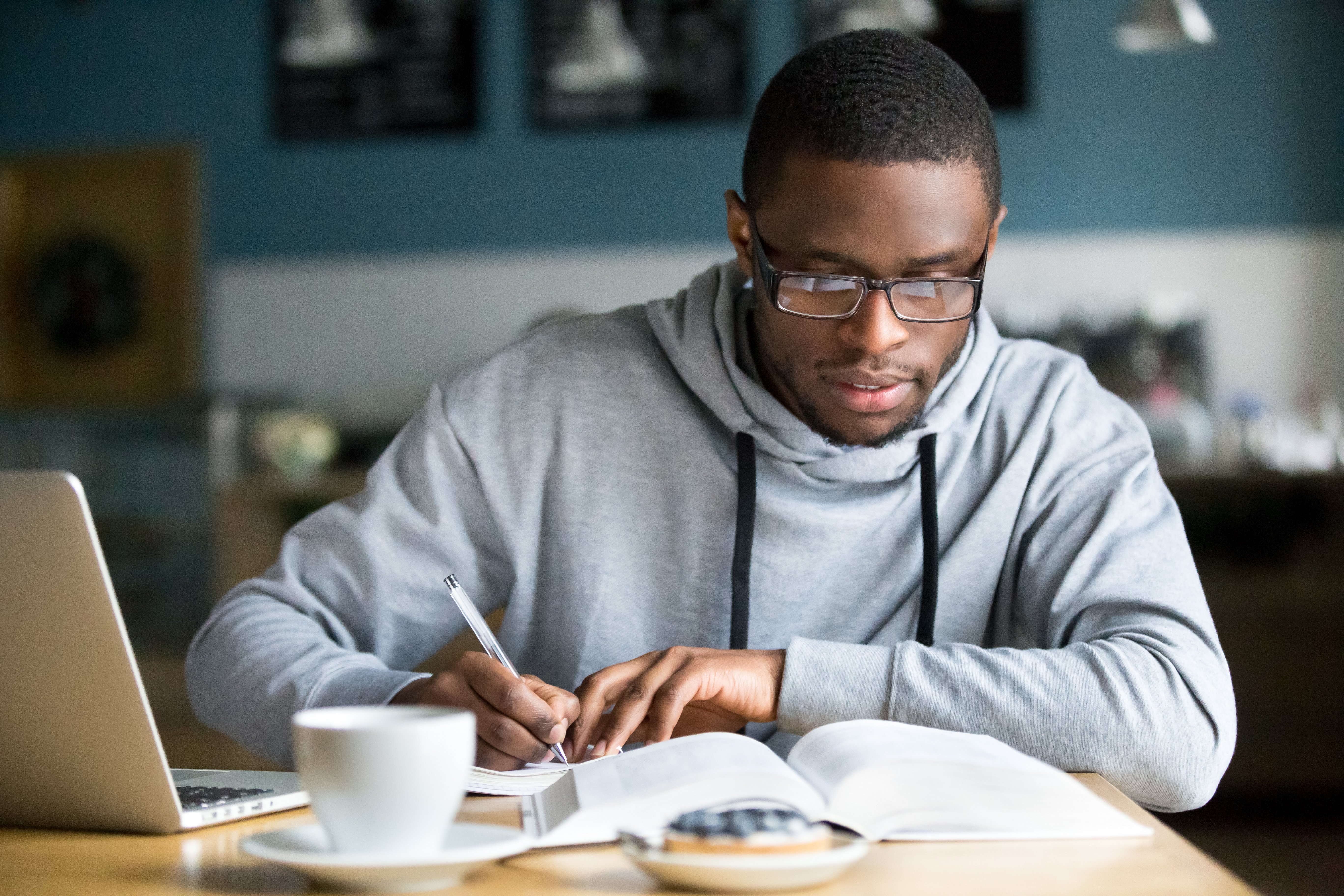 Man studying in coffee shop with laptop and notebook