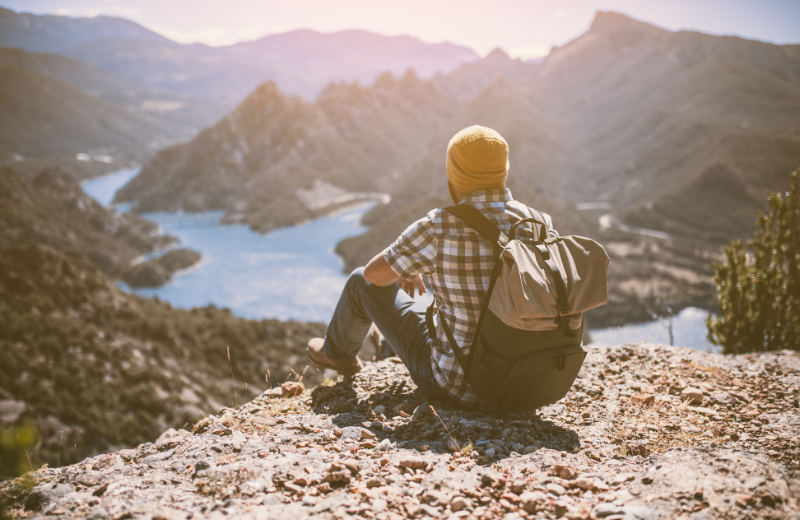 Image of someone sitting on top of a mountain being independent.