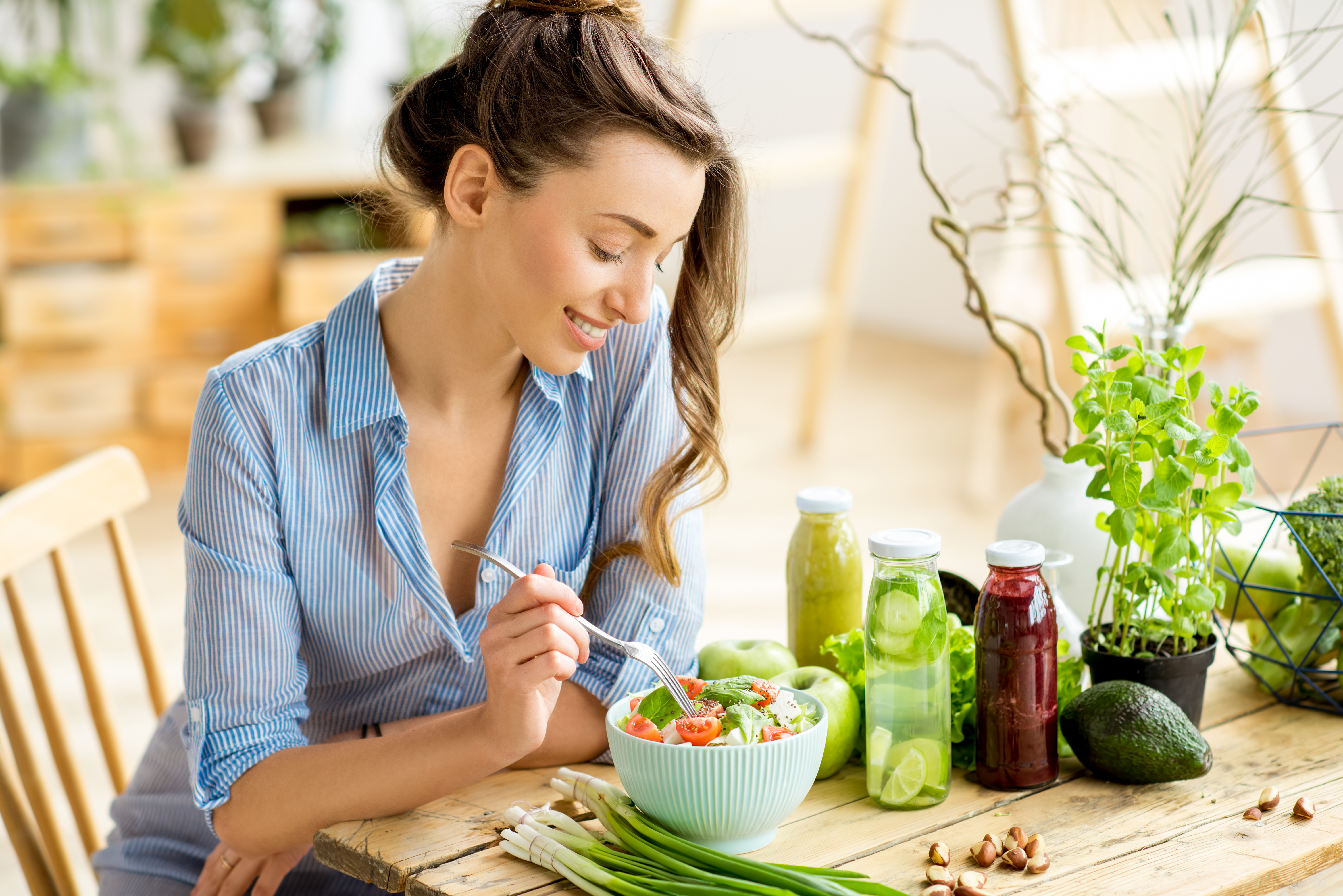 Someone eating a salad with smoothies and vegetables next to them