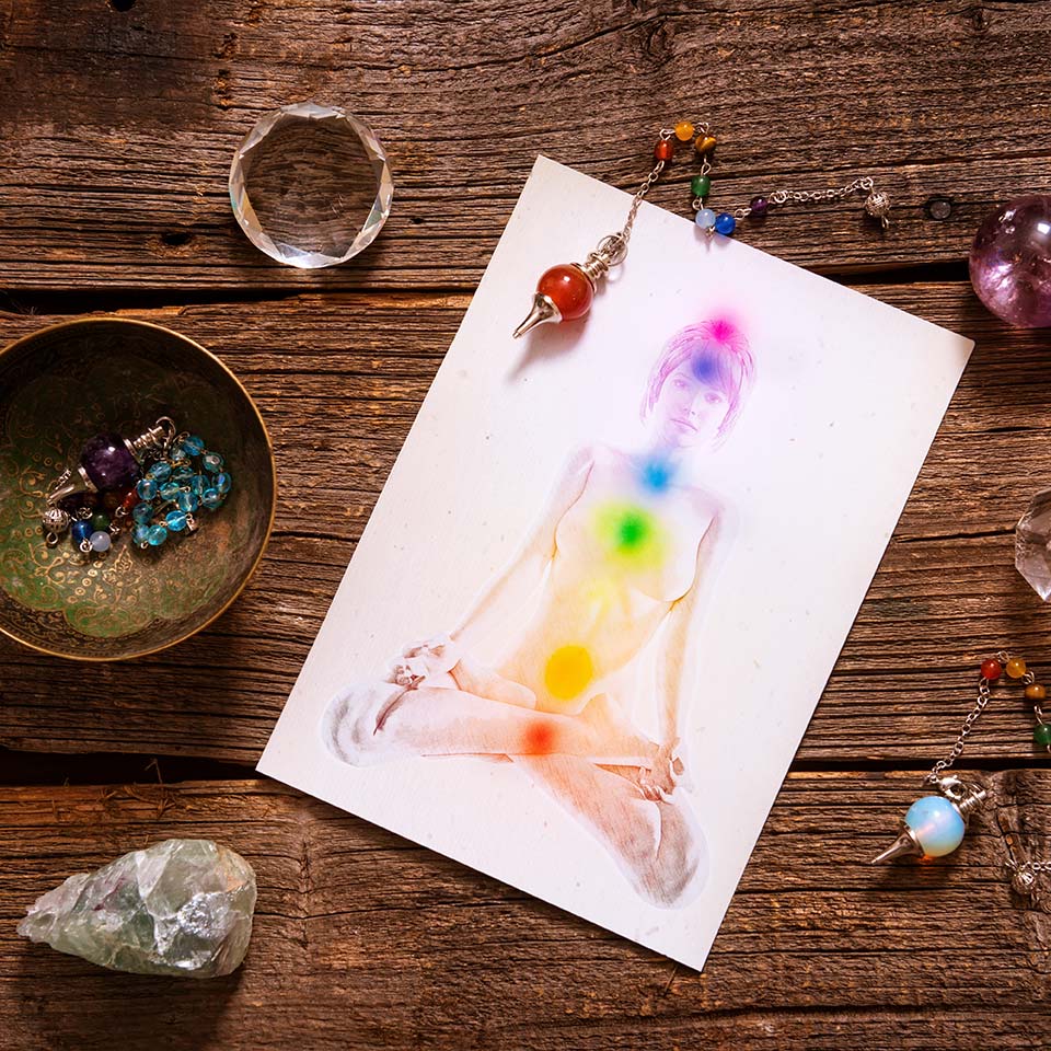 A desk with various chakra and aura healing tools, such as healing stones, pendants, and a diagram of the positions and colours of the chakras